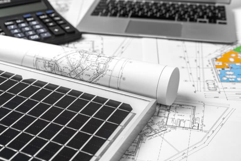 Detailaufnahme eines Solarzellenmoduls auf technischen Plänen, ergänzt durch einen Taschenrechner und einen Laptop, was die Planung und Analyse von erneuerbaren Energien verdeutlicht.
