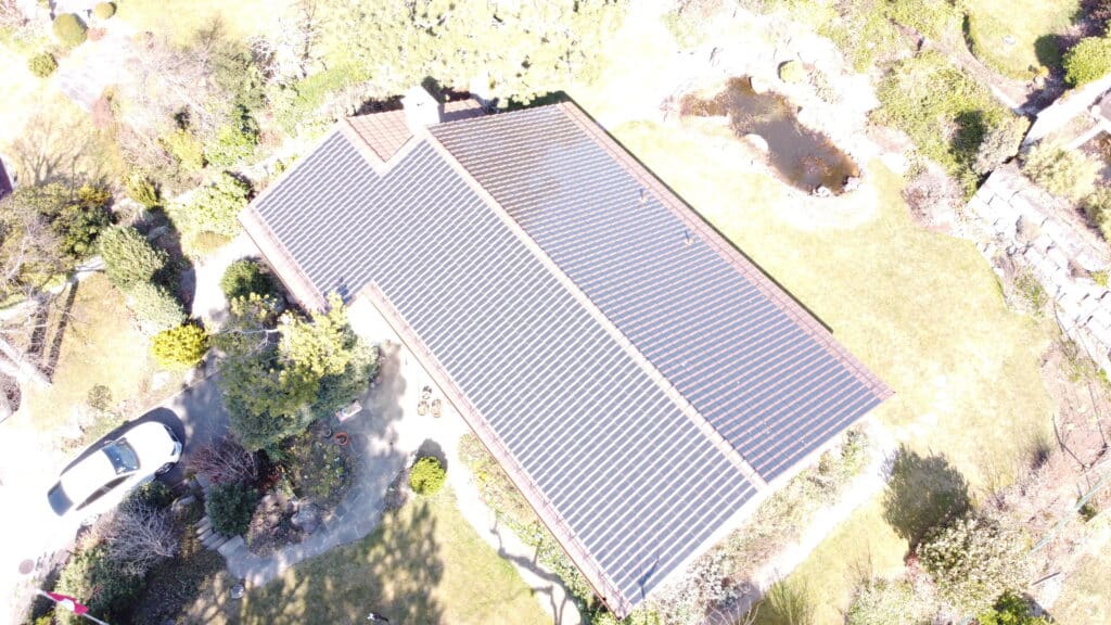 Dachansicht eines Einfamilienhauses mit Solarpanelen, umgeben von einem gepflegten Garten und einem kleinen Teich. Ein Auto steht in der Einfahrt.