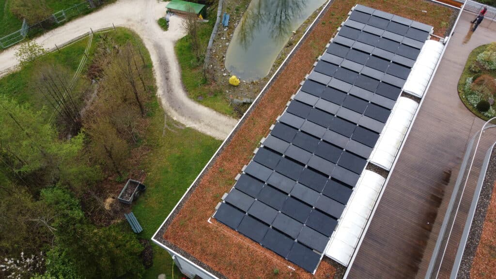Dachansicht mit Photovoltaikanlage, die mehrere Solarpanels zeigt, umgeben von grünen Flächen und einem kleinen Gewässer. Ideal zur Nutzung erneuerbarer Energien in der umliegenden Natur.